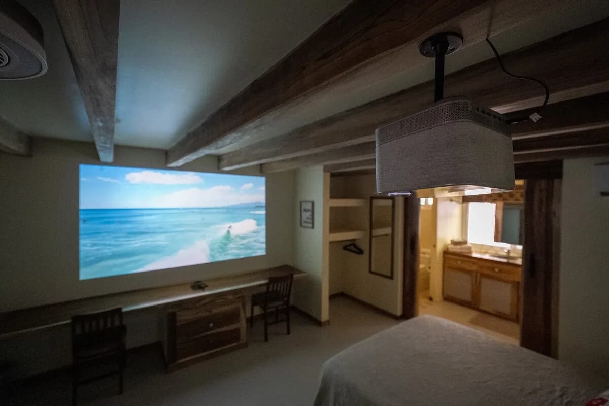 Interior en penumbra con una imagen de mar proyectada en la pared, repisa larga con dos sillas, nicho abierto con perchas y lavabo visible por una puerta.