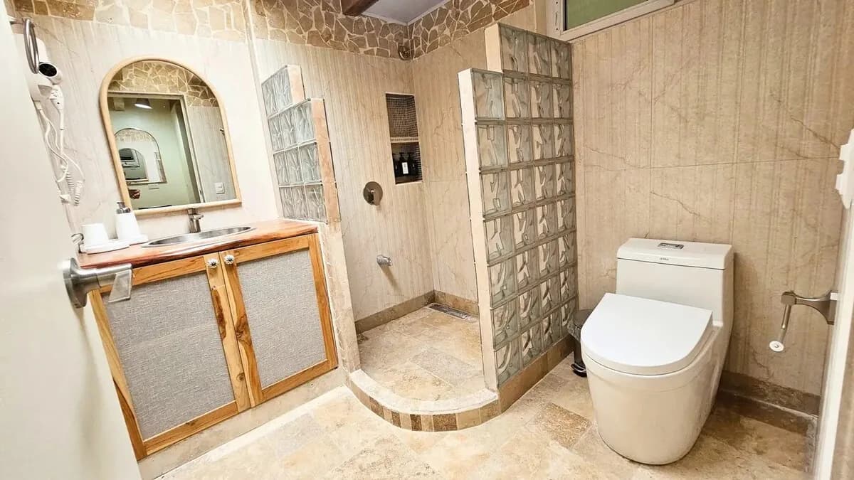 Bathroom viewed from the doorway, with a wooden vanity on the left, a shower between glass blocks, and a toilet on the right.